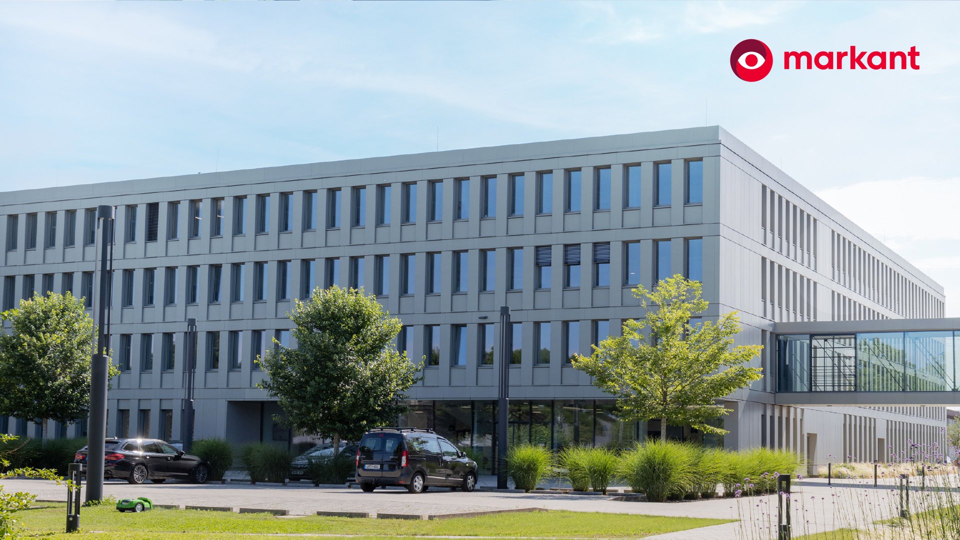 Modernes Bürogebäude von markant mit Grünanlage und parkenden Fahrzeugen