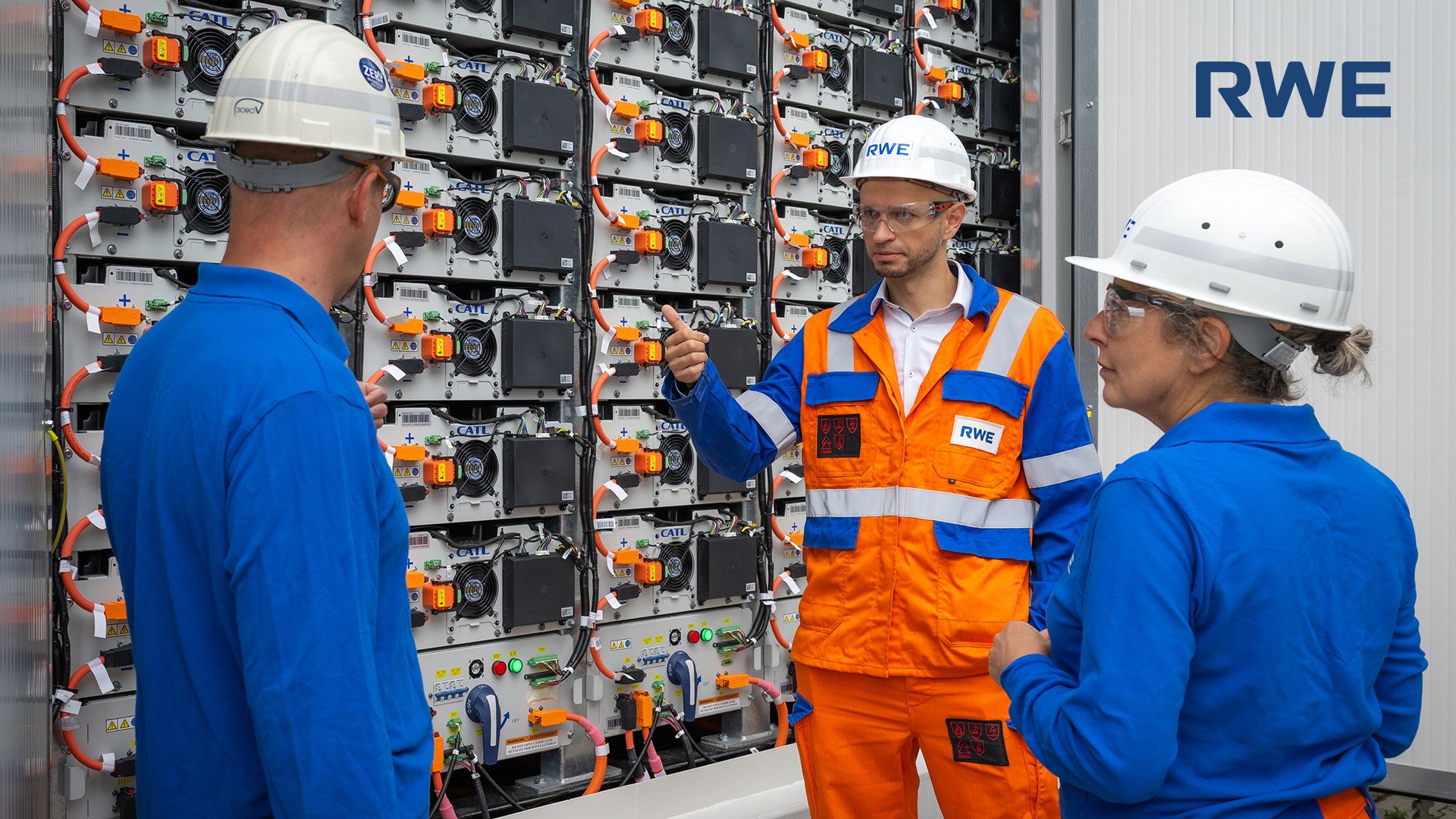 Drei RWE-Mitarbeitende in Schutzausrüstung im Gespräch vor einem Batteriespeicher-System